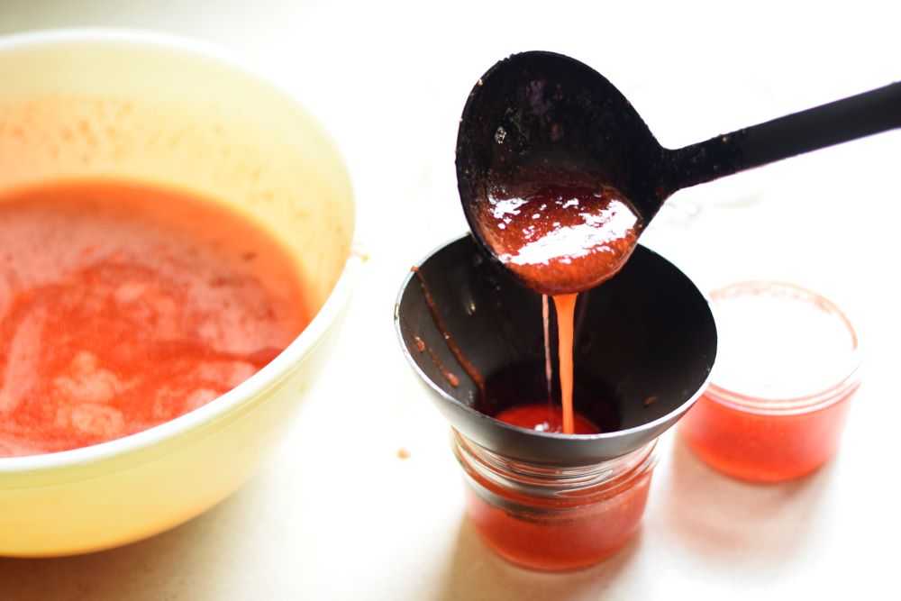 Ladling strawberry freezer jam into jars.