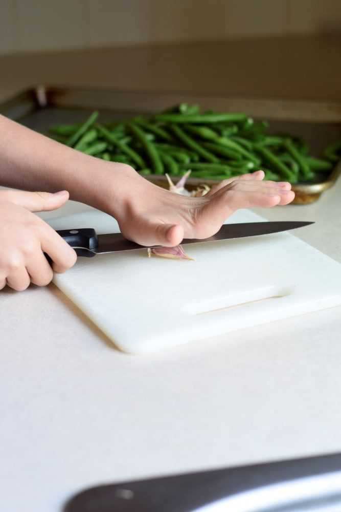 Chopping garlic with green beans in the background.